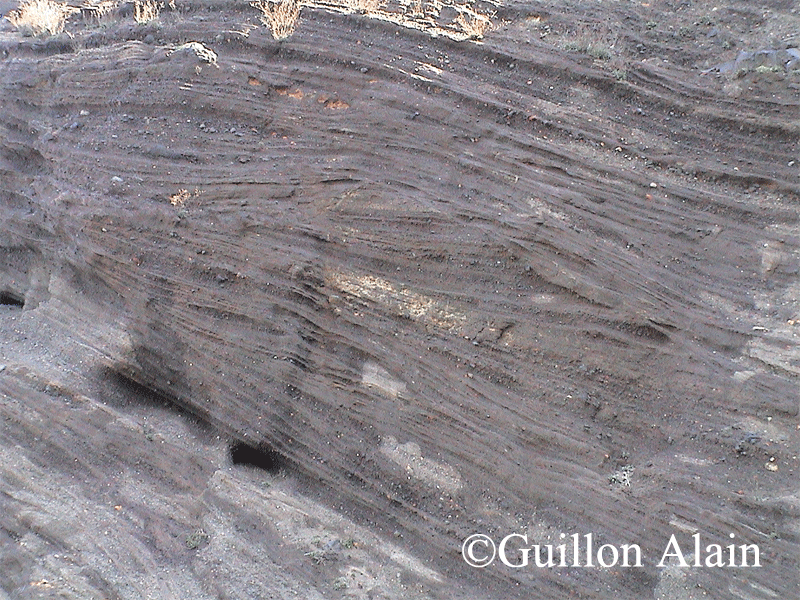 Photo 16 - Plage de la Conque, zone sud.  La vue montre les dépôts de tufs gris avec des érosions mécaniques liées à la force des déferlantes basales, des structures en anti-dune sont aussi visibles (Alain Guillon).